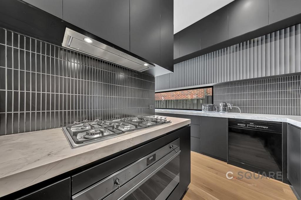 Matte black kitchen with stainless cooktop, rangehood and vertical stacked splashback tiles