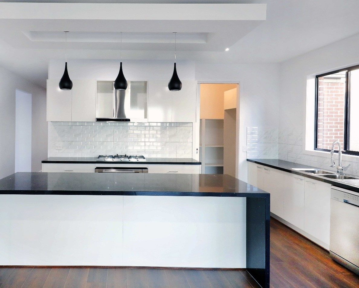 White kitchen with waterfall island, three black pendant lights and a walk-in pantry
